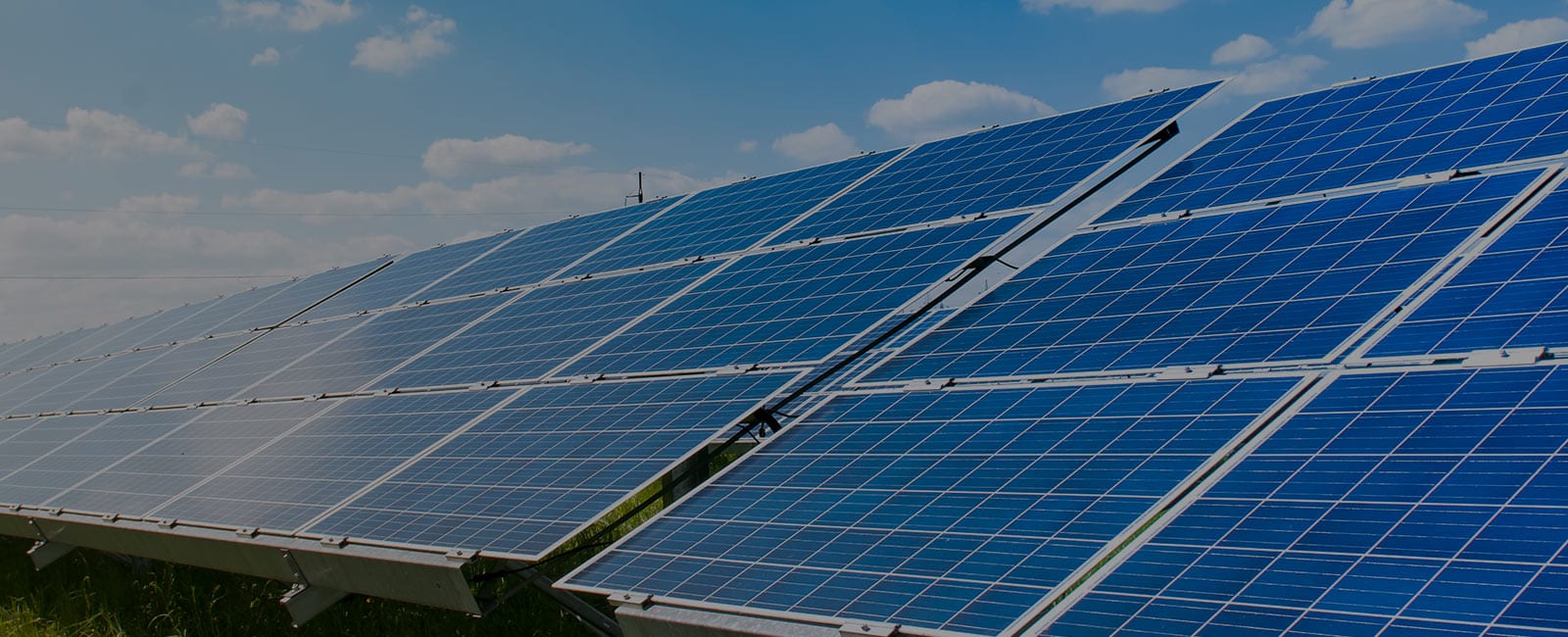 Large array of blue solar panels installed outdoors under a partly cloudy sky, generating renewable energy.