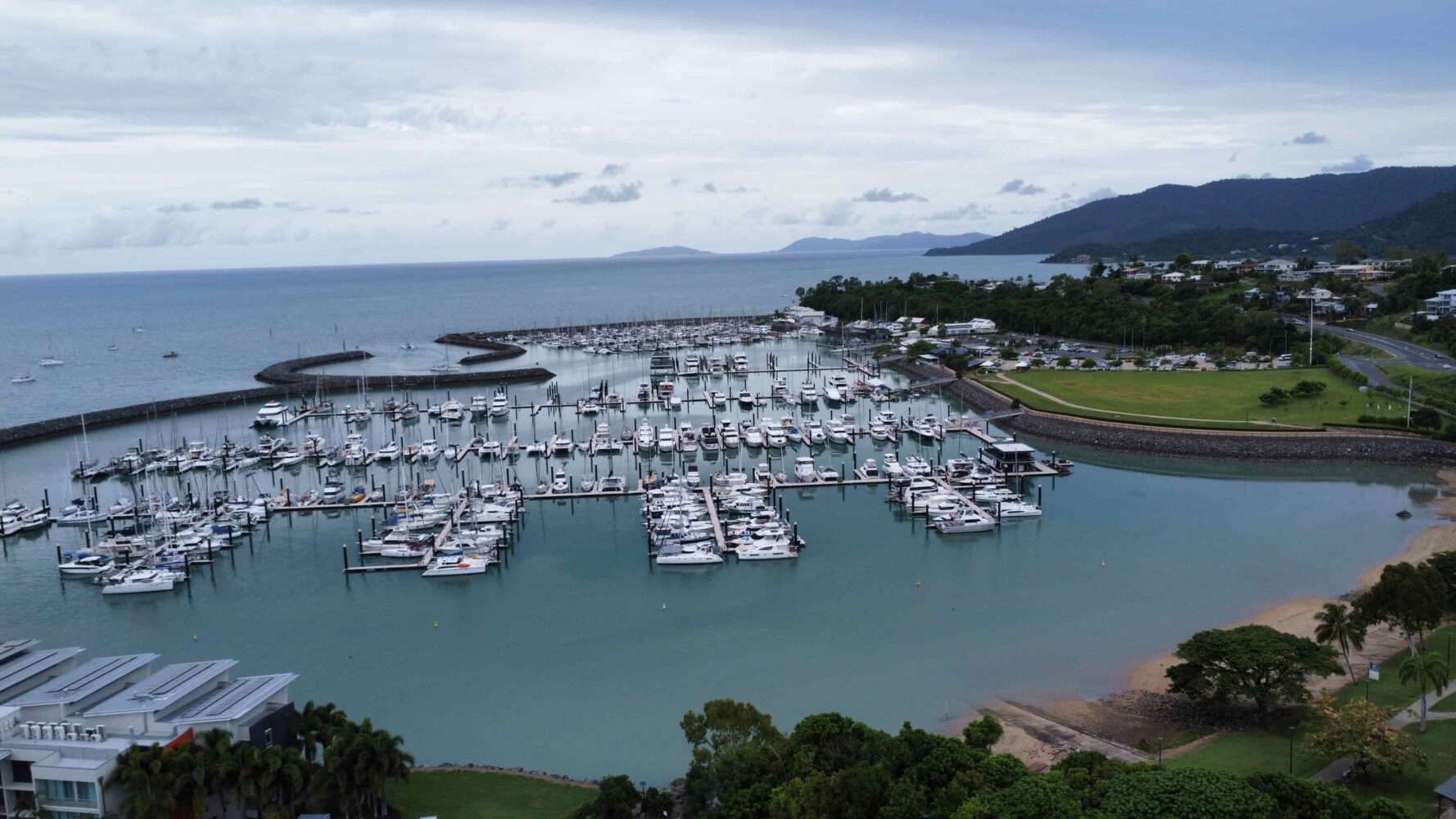 Aerial view of a marina with numerous boats docked in calm waters, surrounded by lush greenery and mountains, with solar panels visible on a nearby rooftop Aerial view of a marina with numerous boats docked in calm waters, surrounded by lush greenery and mountains, with solar panels visible on a nearby rooftop